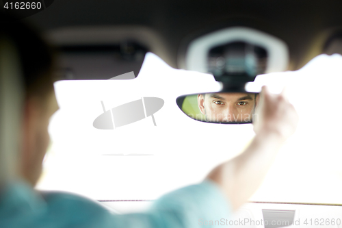 Image of man driving car adjusting rearview mirror