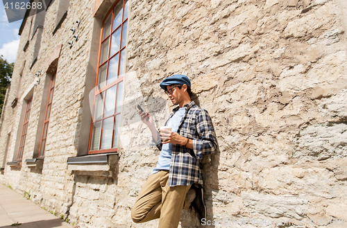 Image of man with smartphone drinking coffee on city street