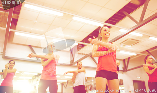 Image of group of smiling people stretching in the gym