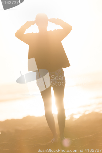 Image of Woman on sandy beach watching sunset.