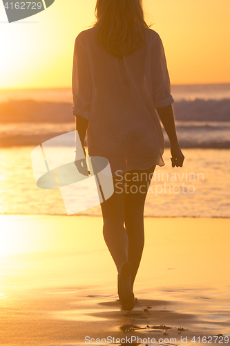 Image of Lady walking on sandy beach in sunset.