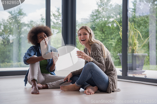 Image of multiethnic women sit on the floor and drinking coffee