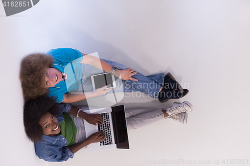 Image of multiethnic couple sitting on the floor with a laptop and tablet