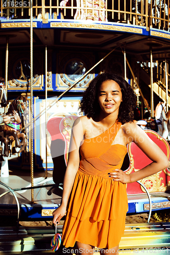 Image of cool real teenage girl with candy near carousels at amusement pa