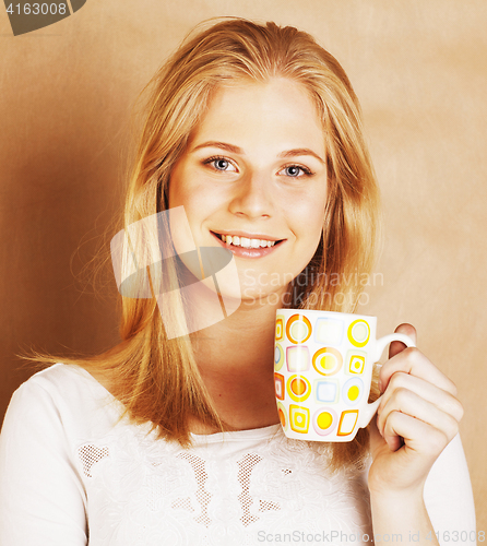 Image of young cute blond girl drinking coffee close up on warm brown bac