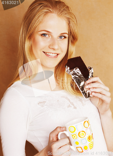 Image of young cute blond girl eating chocolate and drinking coffee close