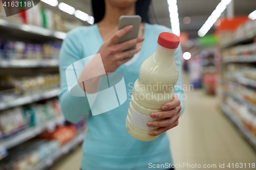 Image of woman with smartphone buying milk at supermarket