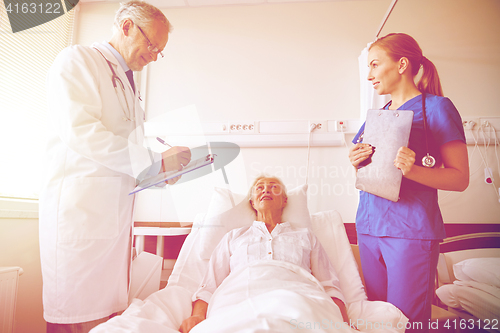 Image of doctor and nurse visiting senior woman at hospital