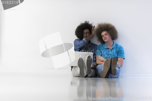 Image of multiethnic couple sitting on the floor with a laptop and tablet