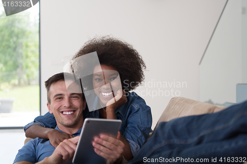 Image of multiethnic couple relaxing at  home with tablet computers