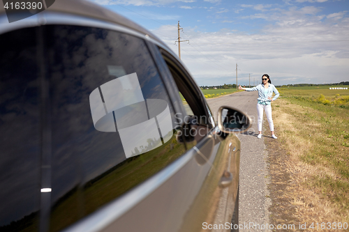 Image of woman hitchhiking and stopping car with thumbs up