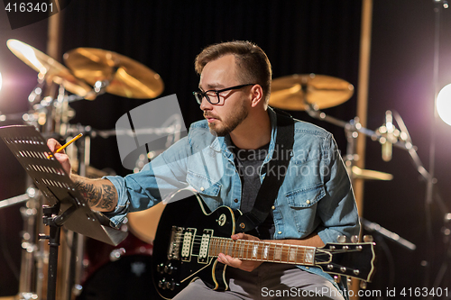 Image of man with guitar writing to music book at studio