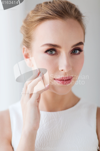 Image of beautiful woman in white dress touching her face