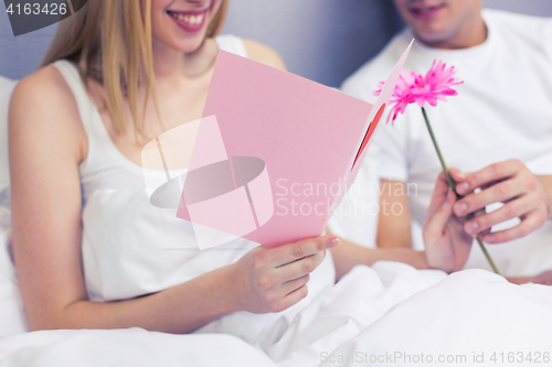 Image of close up of couple in bed with postcard and flower