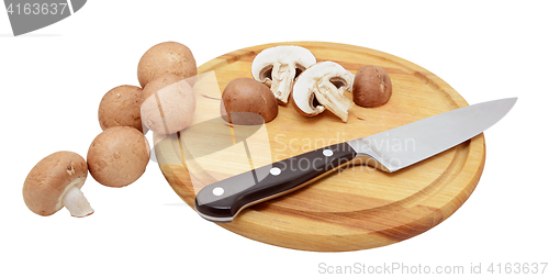 Image of Whole and halved chestnut mushrooms with knife on wooden board