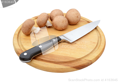 Image of Fresh chestnut mushrooms with sharp knife on a wooden board