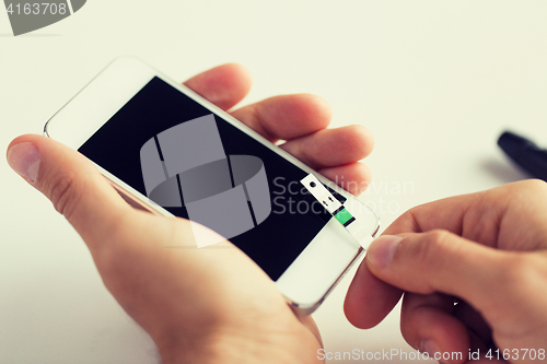 Image of close up of man with smartphone making blood test