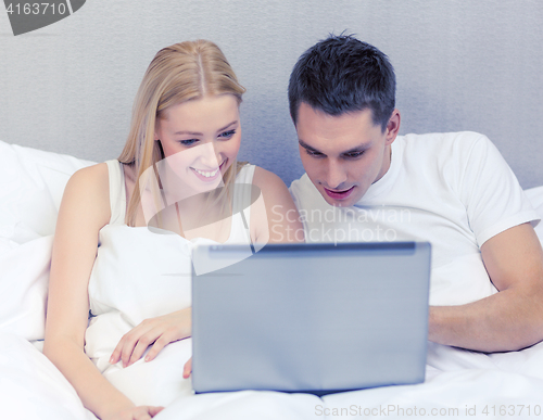 Image of smiling couple in bed with laptop computer