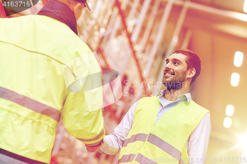 Image of men in safety vests shaking hands at warehouse