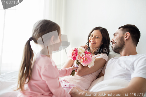 Image of happy girl giving flowers to mother in bed at home