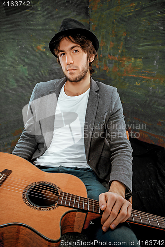 Image of Cool guy sitting with guitar on gray background