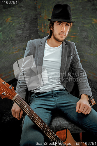 Image of Cool guy sitting with guitar on gray background