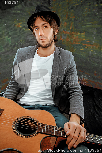 Image of Cool guy sitting with guitar on gray background