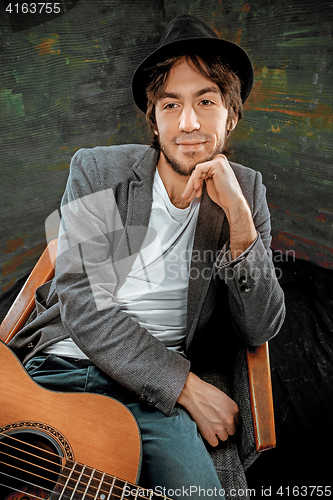 Image of Cool guy sitting with guitar on gray background