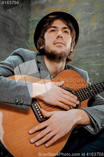 Image of Cool guy sitting with guitar on gray background