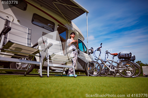 Image of Woman is standing with a mug of coffee near the camper.