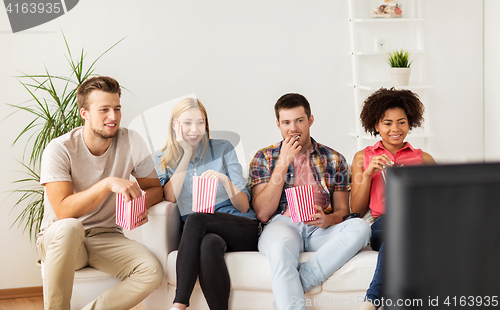 Image of happy friends with popcorn watching tv at home