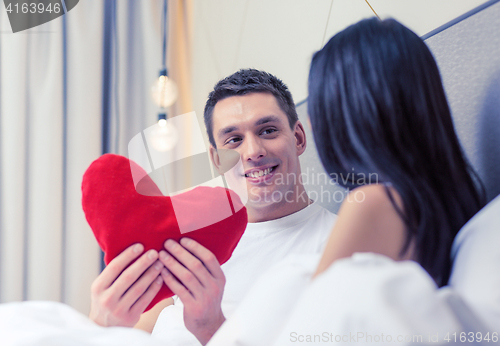 Image of smiling couple in bed with red heart shape pillow