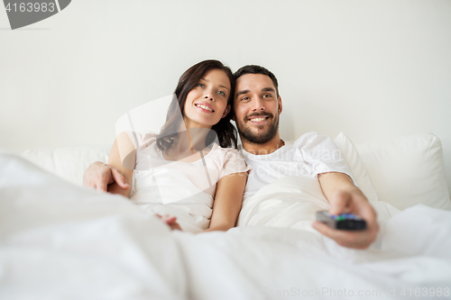 Image of happy couple lying in bed at home and watching tv