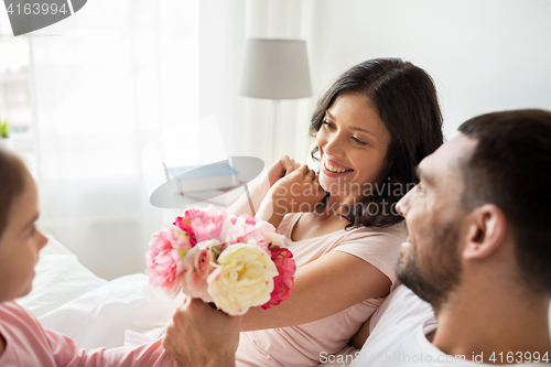 Image of happy girl giving flowers to mother in bed at home