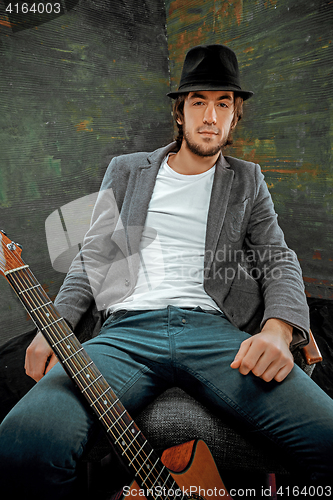 Image of Cool guy sitting with guitar on gray background