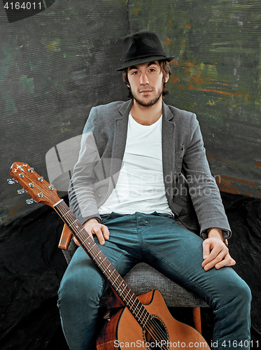 Image of Cool guy sitting with guitar on gray background