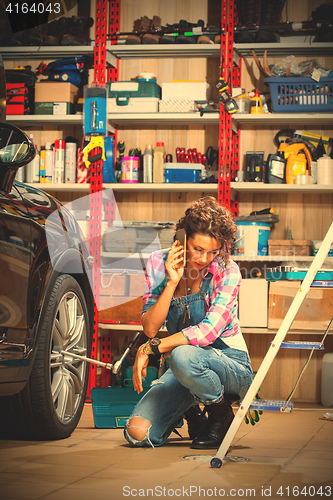 Image of beautiful woman in blue overalls mechanic near the car and talki