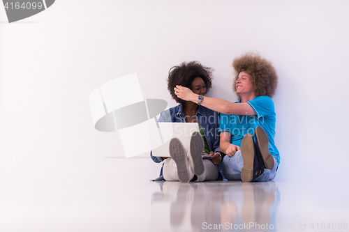 Image of multiethnic couple sitting on the floor with a laptop and tablet