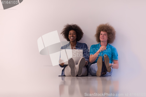 Image of multiethnic couple sitting on the floor with a laptop and tablet
