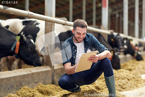 Image of farmer with clipboard and cows in cowshed on farm