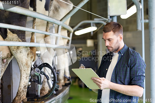 Image of man with clipboard and milking cows on dairy farm