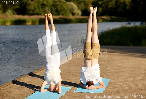 Image of couple making yoga headstand on mat outdoors