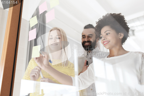 Image of happy creative team writing on stickers at office