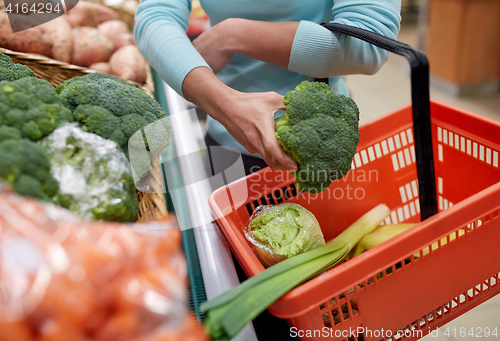 Image of woman with basket buying broccoli at grocery store