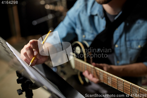 Image of man with guitar writing to music book at studio