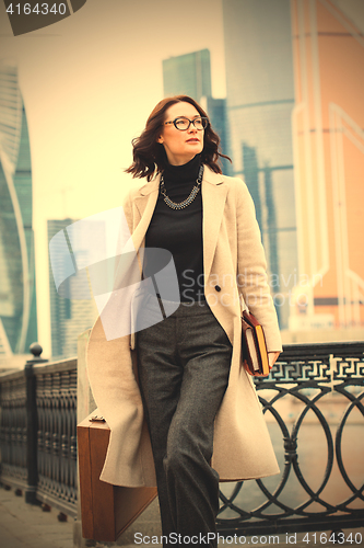 Image of beautiful businesswoman in a light coat, with a wooden case and 