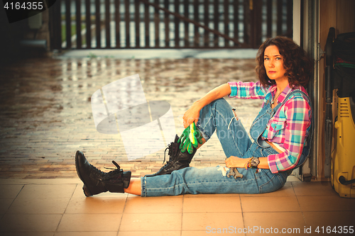 Image of beautiful woman in blue overalls mechanic sitting on the thresho