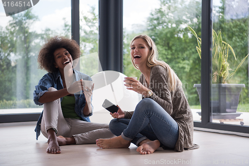 Image of multiethnic women sit on the floor and drinking coffee