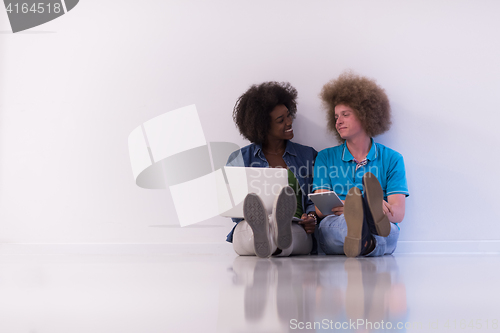 Image of multiethnic couple sitting on the floor with a laptop and tablet