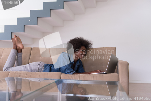 Image of African American woman using laptop on sofa